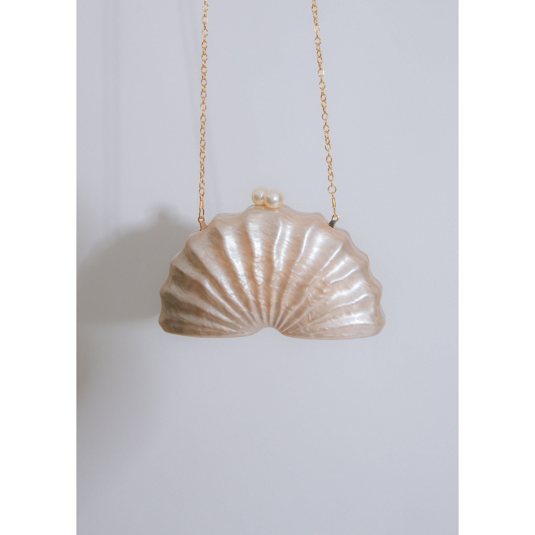 Iridescent seashell shape clutch with luminous pearl accent closure and detachable gold chain strap  